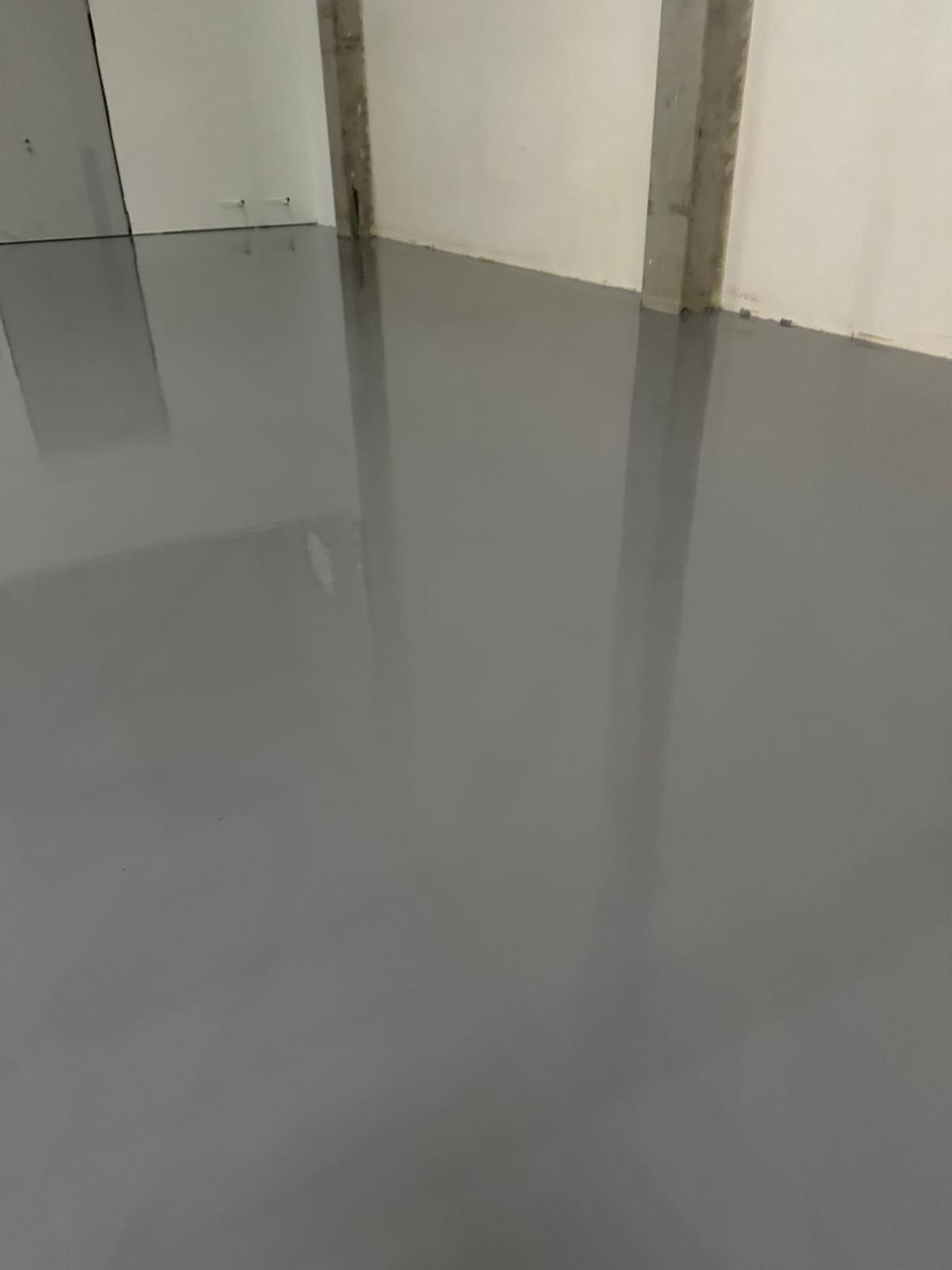 Gładka, szara posadzka w przemysłowym wnętrzu z betonowymi filarami i białymi ścianami, odbijająca światło.