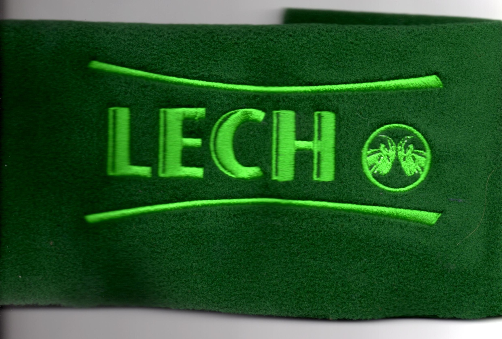 Zielony materiał z wyhaftowanym zielonym napisem 'LECH' i logo w okręgu, otoczony dwiema zielonymi liniami.