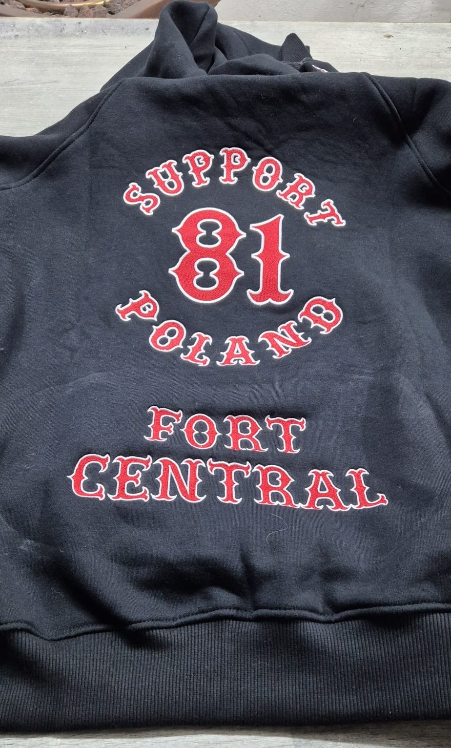 Czarna bluza z kapturem, na plecach czerwony napis 'SUPPORT 81 POLAND FORT CENTRAL' wykonany techniką haftu.