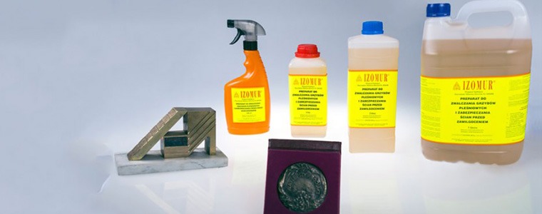 Zestaw produktów marki IZOMER do zwalczania grzybów i zabezpieczania ścian przed zawilgoceniem, prezentowany obok metalowej konstrukcji i medalu w bordowym pudełku na białym tle.
