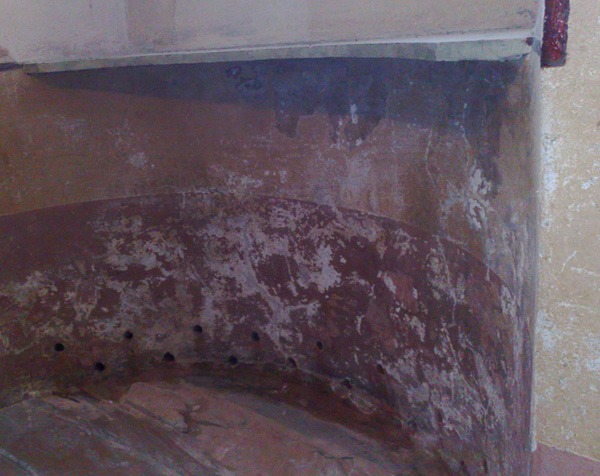 Mokry, uszkodzony fragment ściany z widocznymi zaciekami, plamami i otworami wentylacyjnymi, wskazujący na problem z wilgocią.