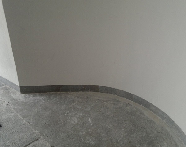 Szara, kamienna podłoga i ściana po zalaniu, widoczne ślady wilgoci i ciemne fugi w dolnej partii ściany.