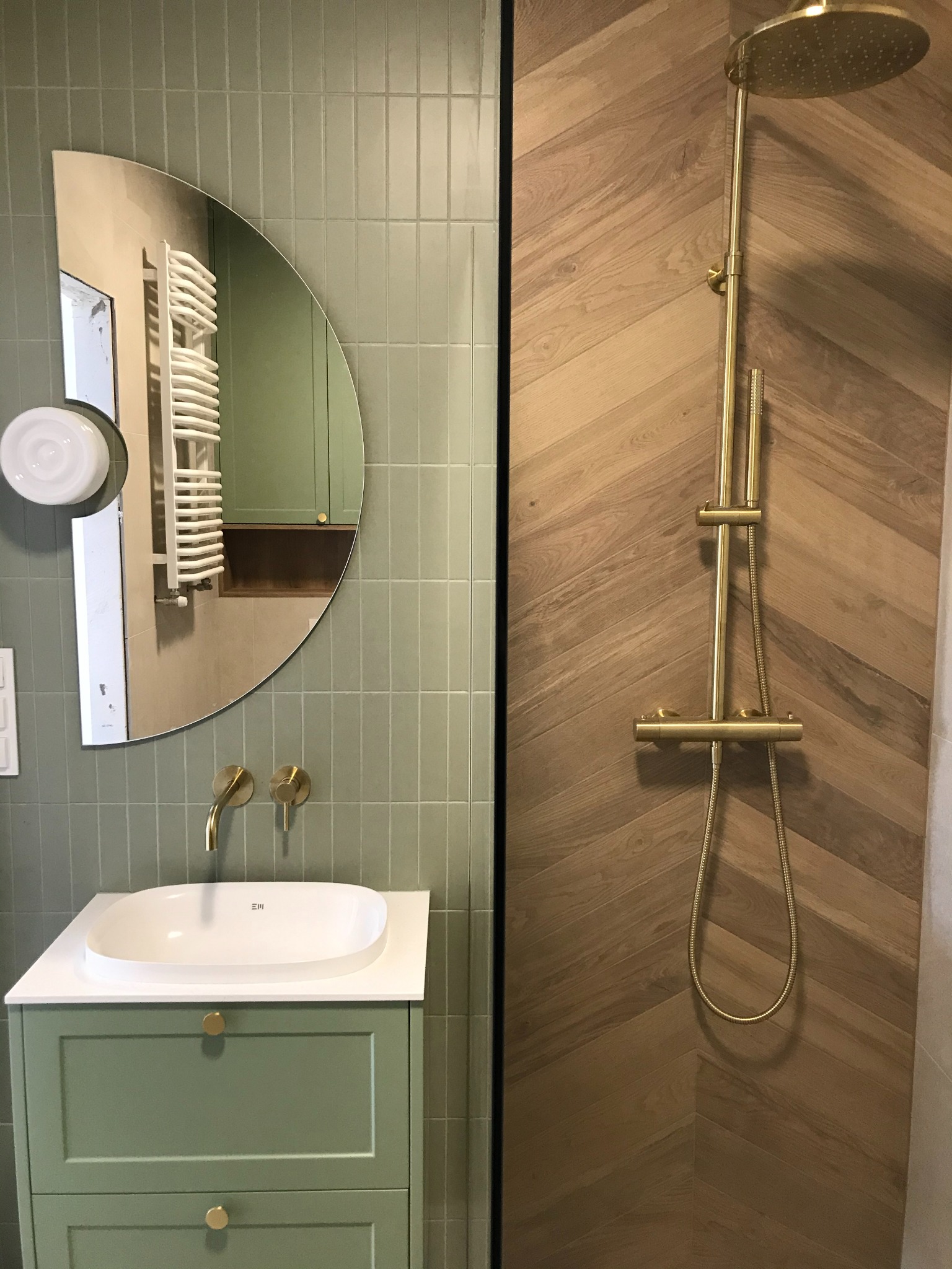 Nowoczesna łazienka z umywalką na szafce w odcieniach zieleni, złotą armaturą i prysznicem ze złotą deszczownicą na ścianie wyłożonej drewnem w jodełkę.