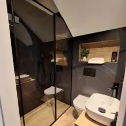 Nowoczesna łazienka z kabiną prysznicową typu walk-in z czarnymi profilami, marmurowymi płytkami i drewnianymi akcentami.