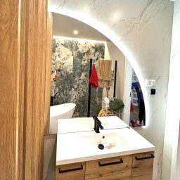 Zakład Szklarski Roman Lizoń - Nowoczesna łazienka z umywalką na szafce z drewnianymi frontami, widok w lustrze z podświetleniem LED w Sosnowcu. Marmurowe płytki na ścianach.