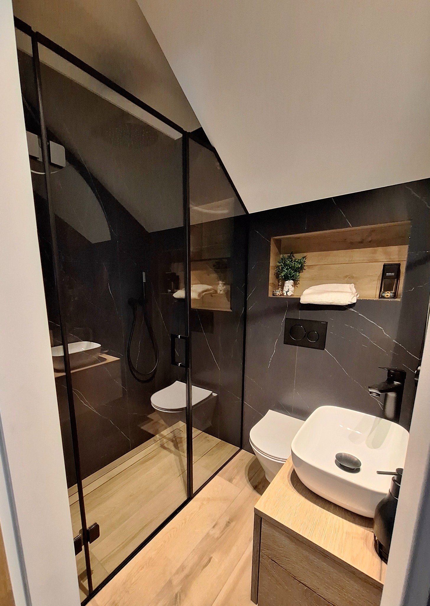 Nowoczesna łazienka z kabiną prysznicową typu walk-in z czarnymi profilami, marmurowymi płytkami i drewnianymi akcentami.