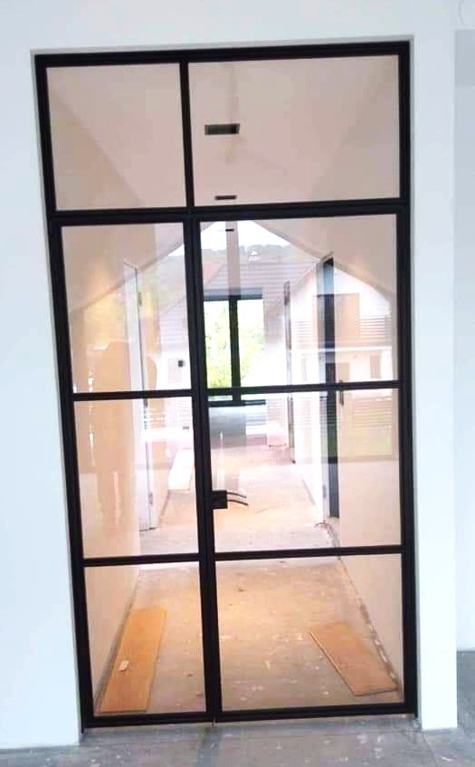 Nowoczesne drzwi wewnętrzne z czarną ramą i szklanymi panelami, widok na korytarz w domu jednorodzinnym, minimalistyczny design, jasne wnętrze.