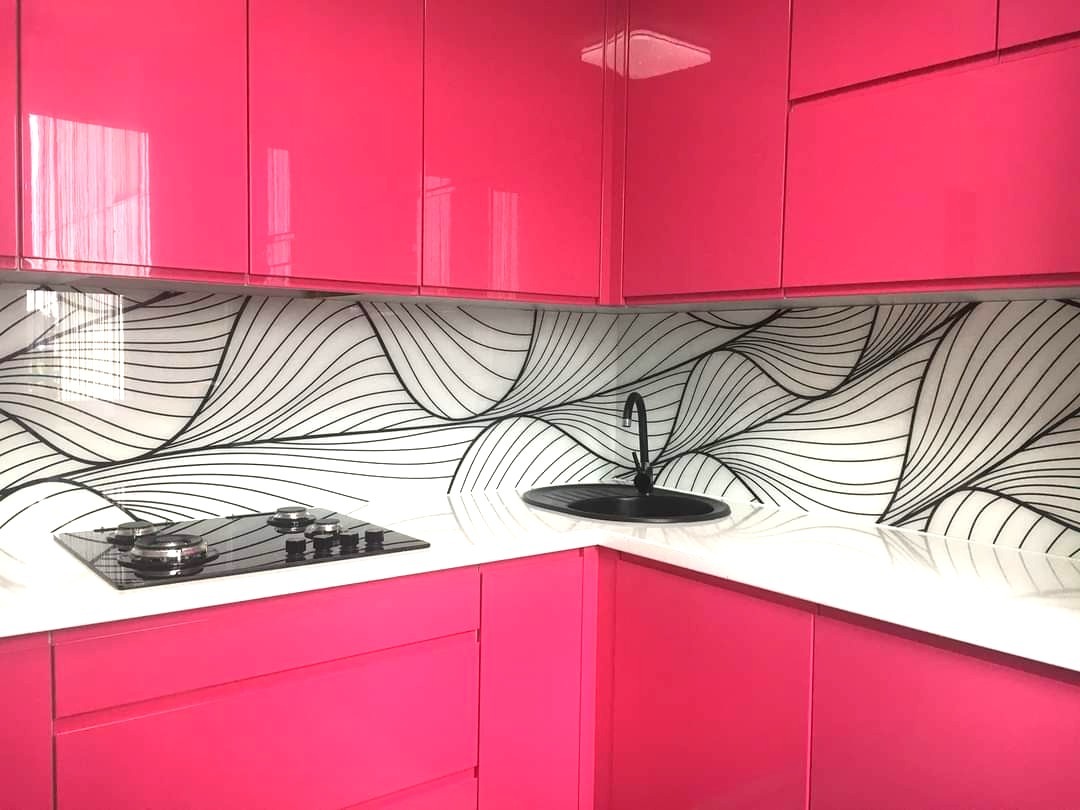Różowa kuchnia z ozdobnym panelem szklanym nad blatem. Czarna armatura i płyta grzewcza. Minimalistyczny design z abstrakcyjnym wzorem fal.