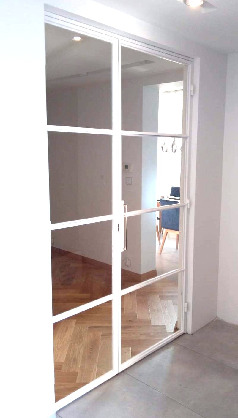 Nowoczesne dwuskrzydłowe drzwi z białymi szprosami, dzielące przestrzeń, widok na parkiet ułożony w jodełkę i minimalistyczne wnętrze.