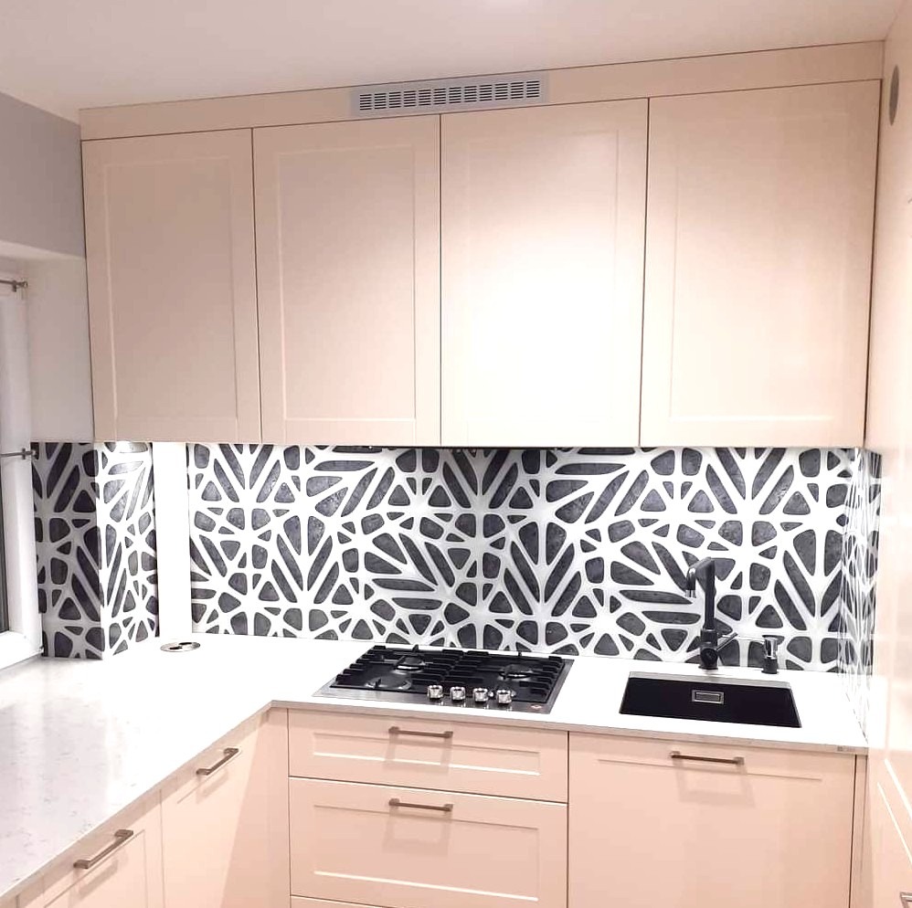 Kuchnia z beżowymi szafkami i blatem, czarną płytą gazową i zlewozmywakiem. Ściana nad blatem wykończona panelami z geometrycznym wzorem.