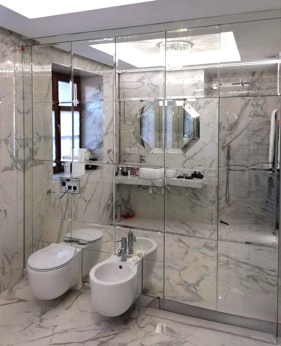 Elegancka łazienka z lustrzanymi panelami ściennymi, odbijającymi światło i powiększającymi przestrzeń. Marmurowe wykończenie podłogi i ścian.