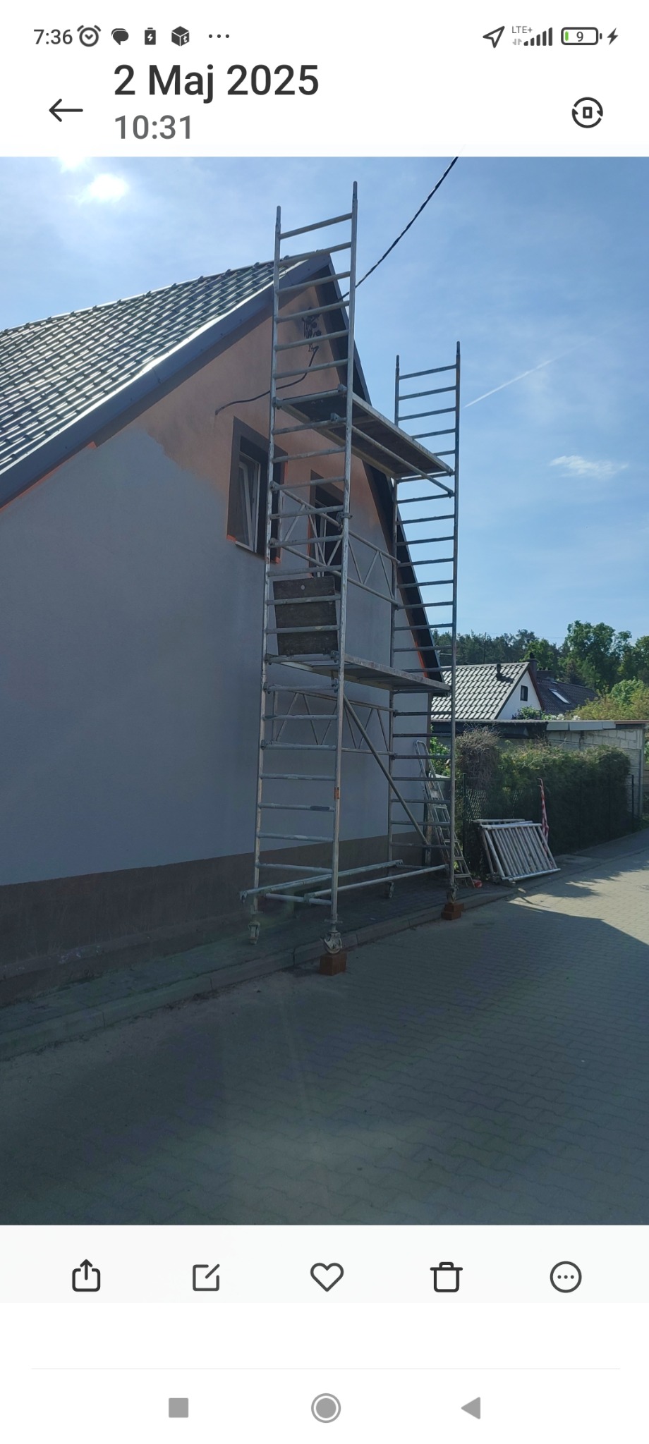 Dom w trakcie malowania elewacji, widoczne rusztowanie i fragment pomalowanej ściany na jasny kolor. Część elewacji w kolorze pomarańczowym.