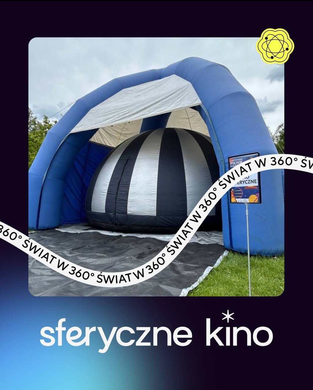 Mobilna kopuła sferyczna w plenerze, z niebieską konstrukcją i czarno-białym wnętrzem. Tablica informacyjna obok wejścia. Widok z zewnątrz, trawa w tle.