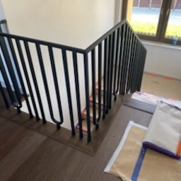TMM SPAW YURII BUDZAN - Nowoczesne schody z czarną, metalową balustradą o pionowych szczeblach, widoczne z góry, z zabezpieczonymi stopniami i podłogą. Minimalistyczny design.