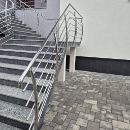 TMM SPAW YURII BUDZAN - Zewnętrzne schody z szarego granitu z nowoczesną, błyszczącą balustradą ze stali nierdzewnej. Widok z dołu, na pierwszym planie kostka brukowa.