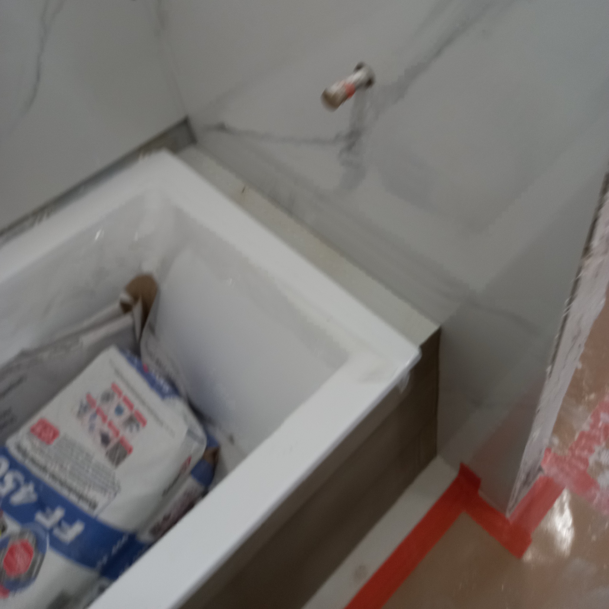 Wnęka z workami zaprawy i fragmentem wykończonej ściany z białych, marmurkowych płytek. Widoczny etap prac wykończeniowych w łazience.
