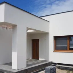 Nowoczesny dom jednorodzinny z białą elewacją, drewnianą stolarką okienną i minimalistycznym wejściem z kolumnami, widoczne kostki brukowe przed wejściem.