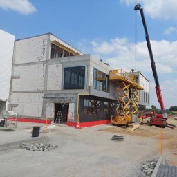 DARWO SP. J. - Wznoszenie dwukondygnacyjnego budynku z betonu komórkowego z elementami konstrukcji stalowej, widoczny żuraw teleskopowy oraz podnośnik nożycowy, teren budowy w trakcie prac wykończeniowych.