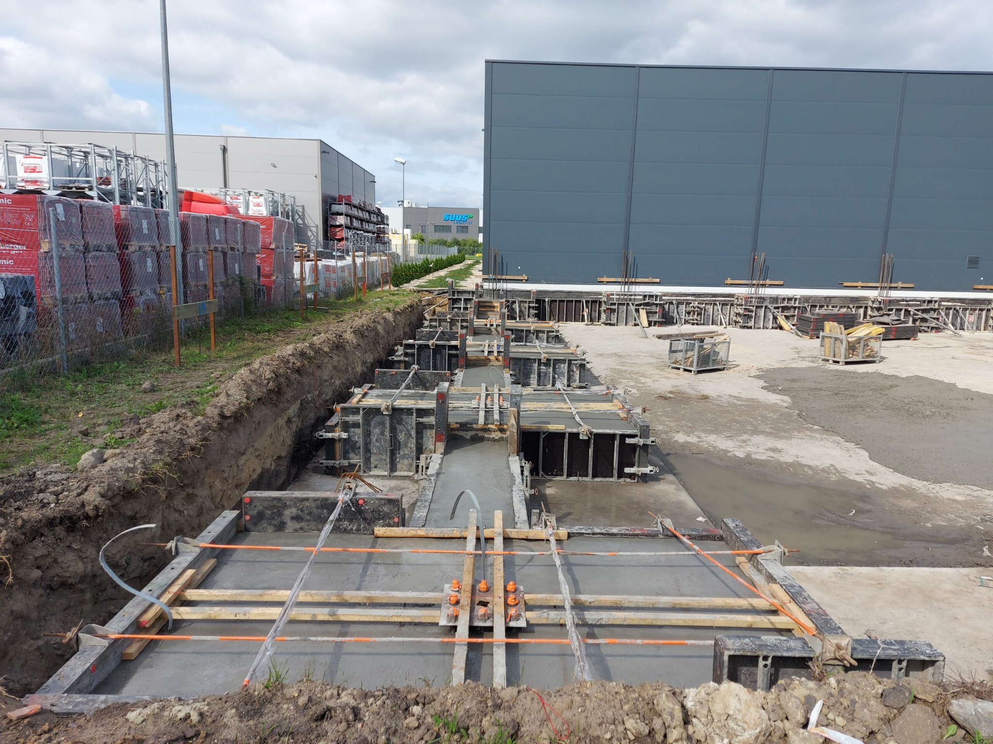 Przygotowanie fundamentów pod budynek przemysłowy, widoczne szalunki zalane betonem, w tle budynki magazynowe.