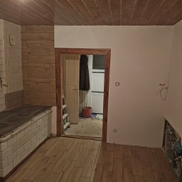 Usługi remontowo budowlane - Wnętrze w trakcie remontu: drewniana boazeria na suficie i ścianie, nowa podłoga z paneli imitujących drewno, stara kuchnia kaflowa, instalacje elektryczne i hydrauliczne częściowo odsłonięte...