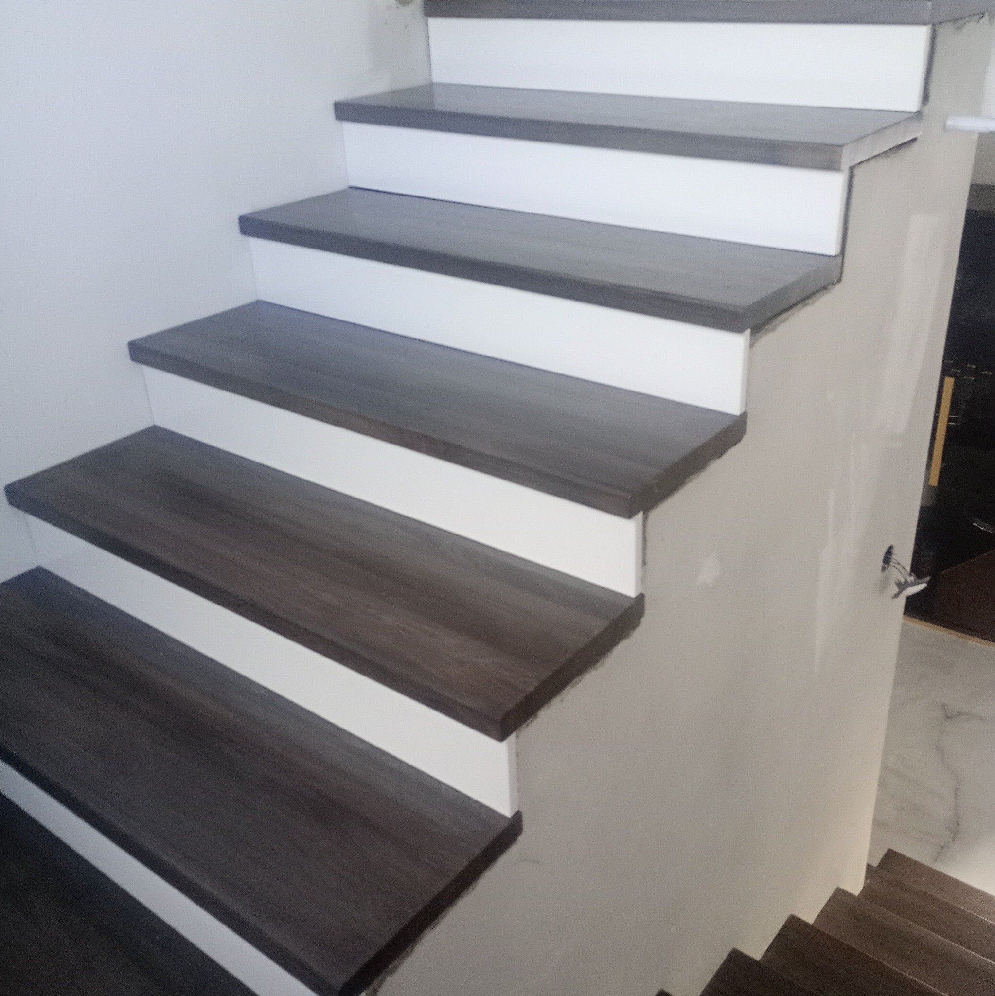 Nowoczesne schody drewniane z białymi podstopnicami i ciemnobrązowymi stopniami, widok z dołu, ściany w surowym stanie.