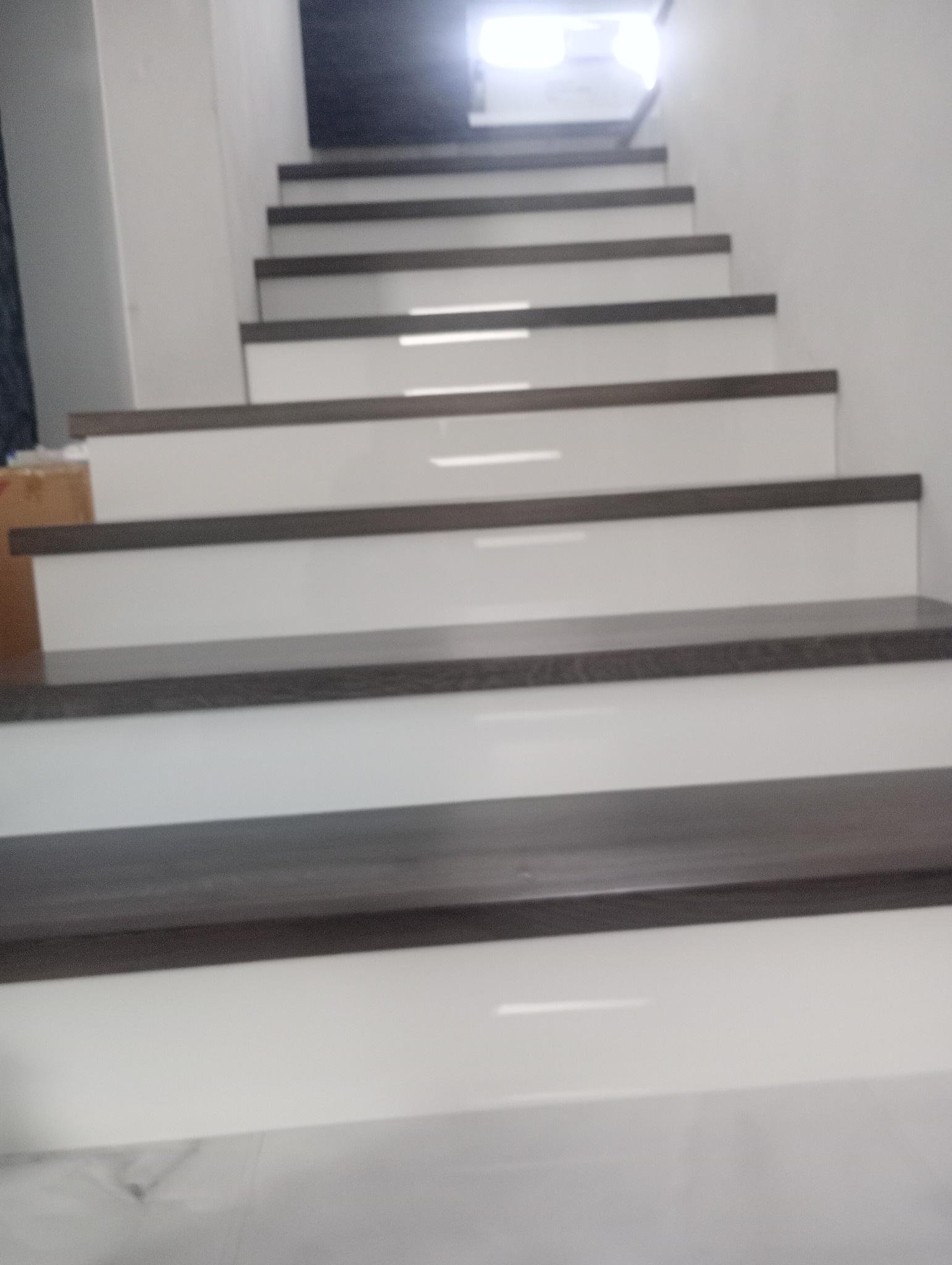 Nowoczesne schody z białymi stopnicami i ciemnobrązowymi krawędziami, widziane z dołu. Minimalistyczny design, jasne wnętrze, schody prowadzą w górę.