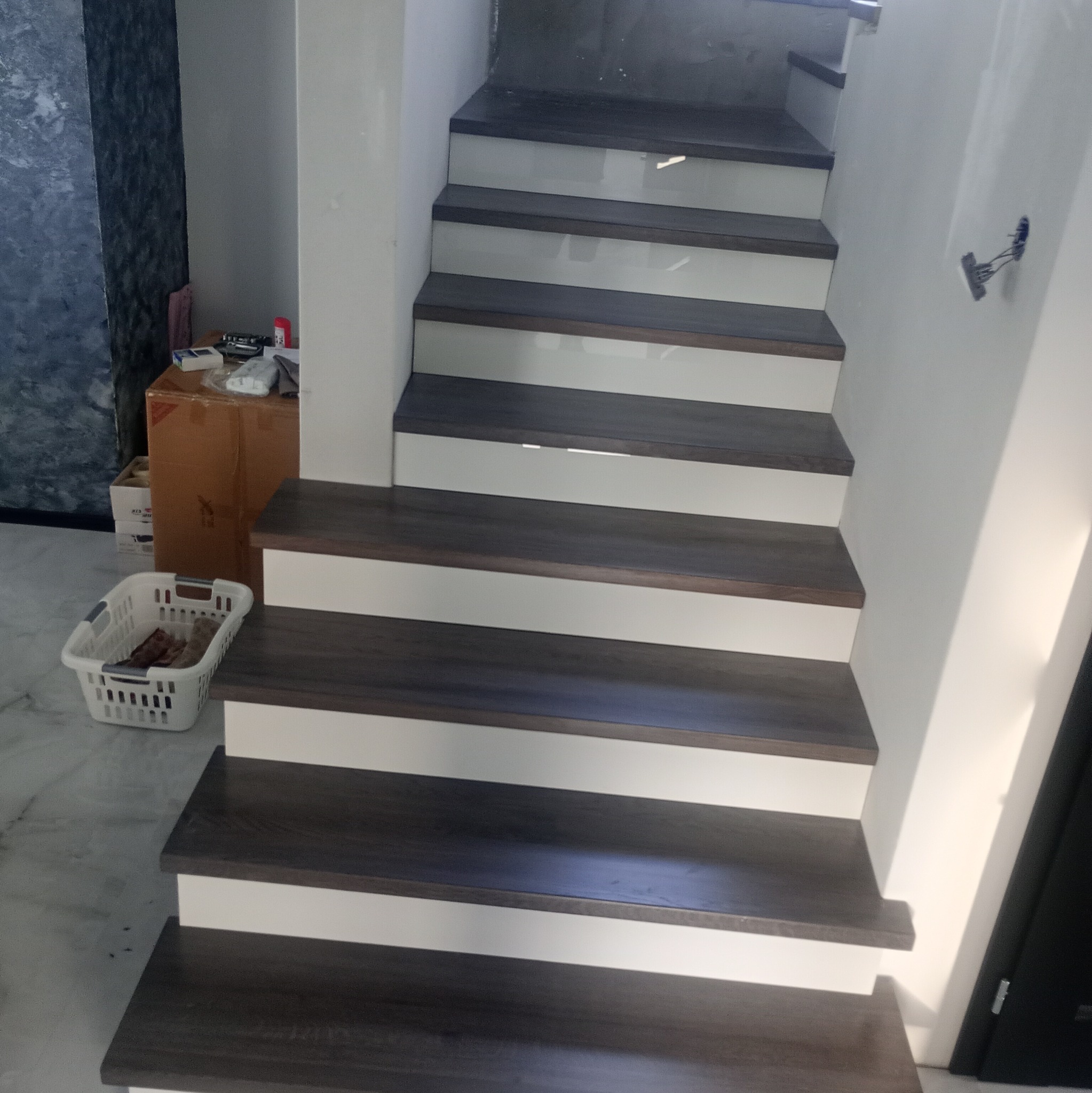 Nowoczesne schody z ciemnego drewna z białymi podstopnicami w jasnym wnętrzu. Widoczne detale wykończenia i minimalistyczny design.