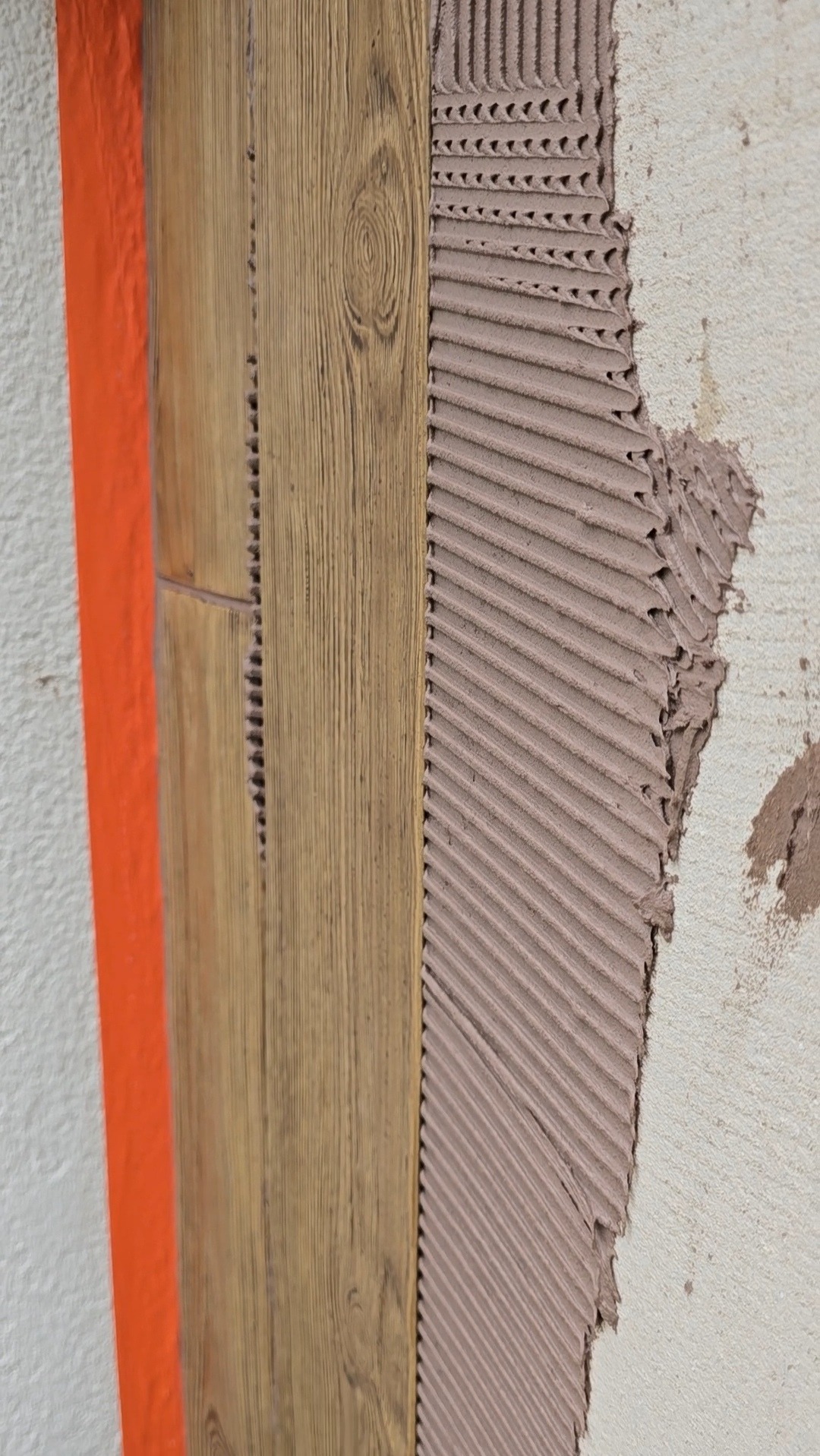 Montaż paneli elewacyjnych z imitacją drewna na ścianie z nałożonym klejem. Widoczne wyżłobienia kleju i pomarańczowe zabezpieczenie.