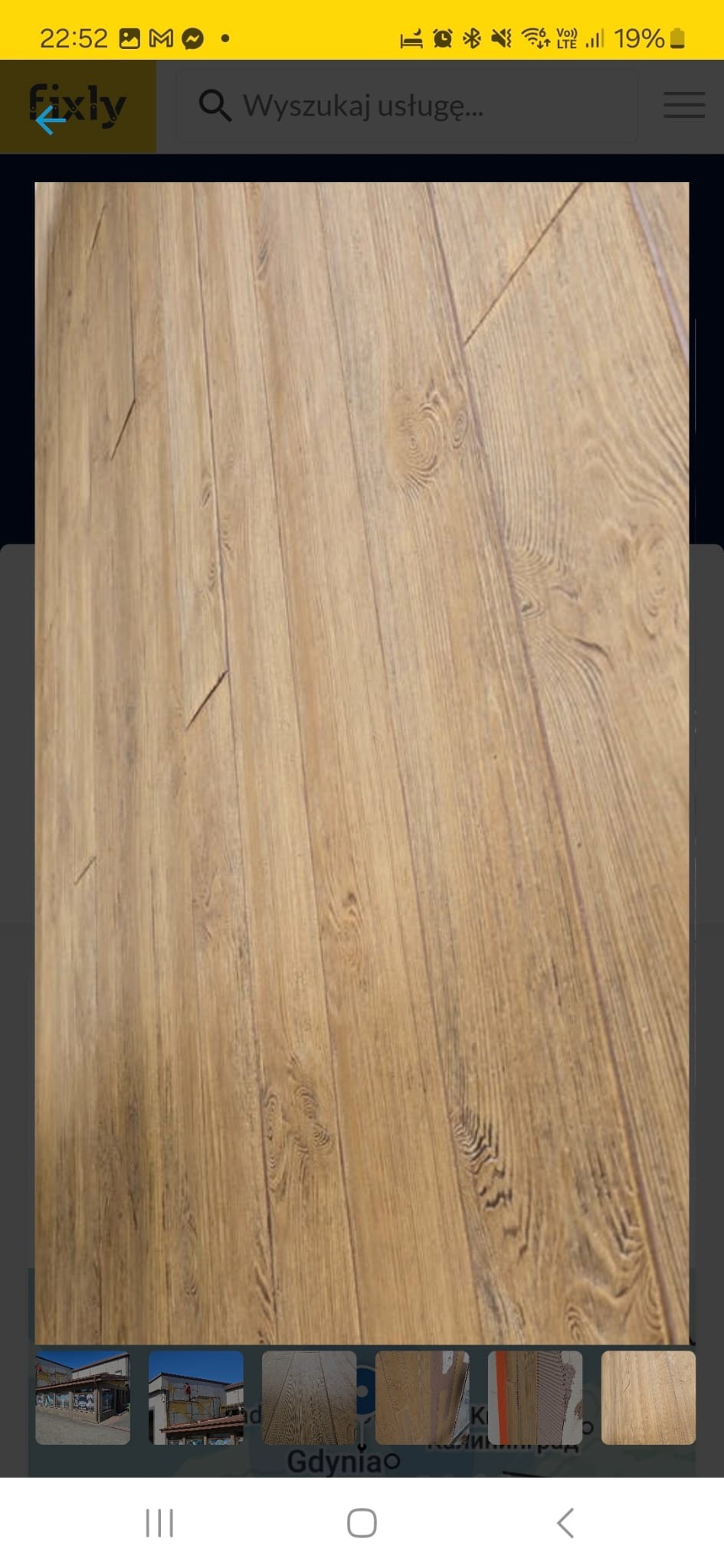 Ukończona podłoga z paneli w odcieniach brązu, imitująca drewno. Widok z góry, lekko pod kątem, ukazujący strukturę i ułożenie paneli. Ciepłe oświetlenie podkreśla fakturę.