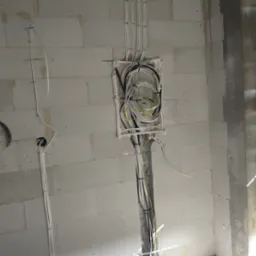 Puszka elektryczna podtynkowa wypełniona przewodami w ścianie z betonu komórkowego; kable prowadzone pionowo w dół i w górę, zabezpieczone uchwytami.