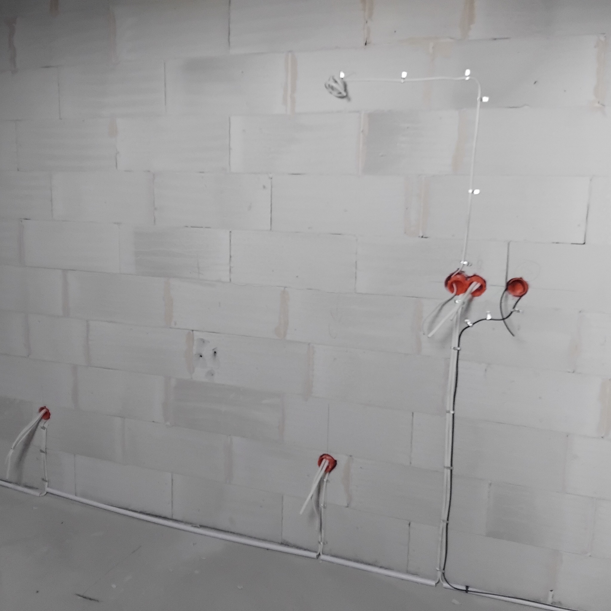 Surowa ściana z betonu komórkowego z poprowadzonymi przewodami elektrycznymi w peszlach i puszkach instalacyjnych.