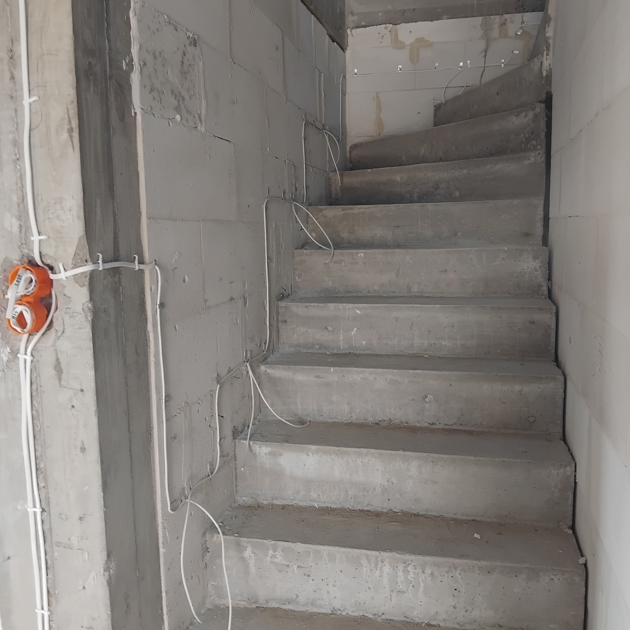 Surowe schody betonowe w trakcie budowy w Łomży, z widocznymi przewodami elektrycznymi prowadzonymi po ścianie i puszką instalacyjną.