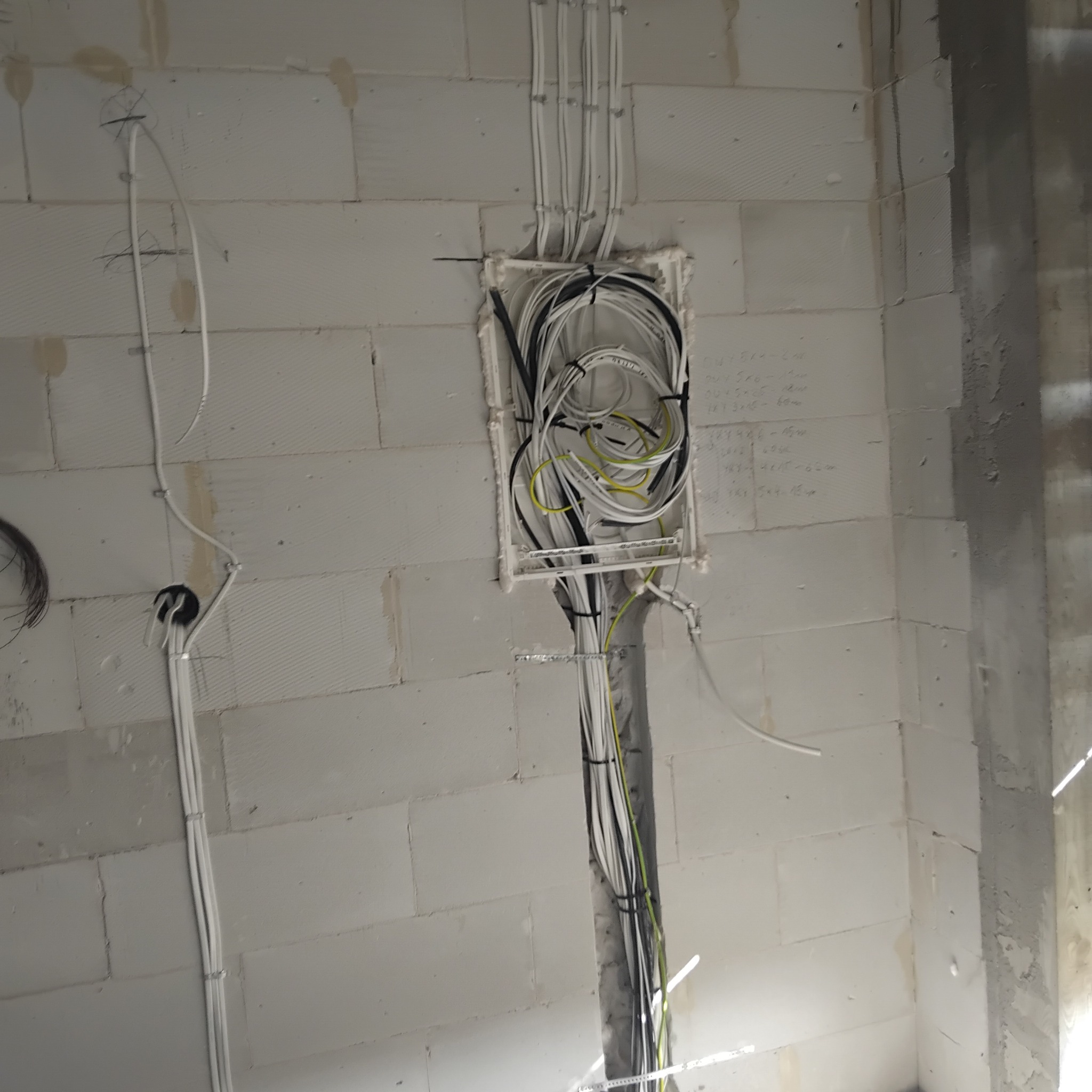 Puszka elektryczna podtynkowa wypełniona przewodami w ścianie z betonu komórkowego; kable prowadzone pionowo w dół i w górę, zabezpieczone uchwytami.