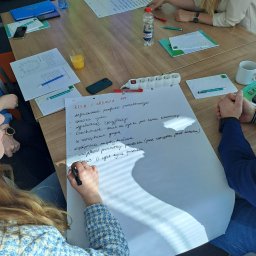 Akademia Marketingu KFK - Grupa osób przy stole podczas burzy mózgów, zapisująca na dużej kartce zadania związane z analizą rynku i produktem.