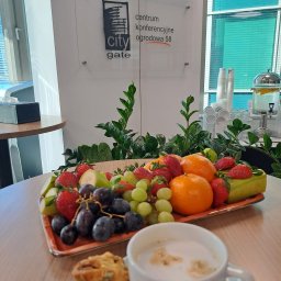 Akademia Marketingu KFK - Stół w sali konferencyjnej z owocami, ciastkiem i kawą, w tle logo centrum konferencyjnego City Gate i dystrybutor wody z cytryną.