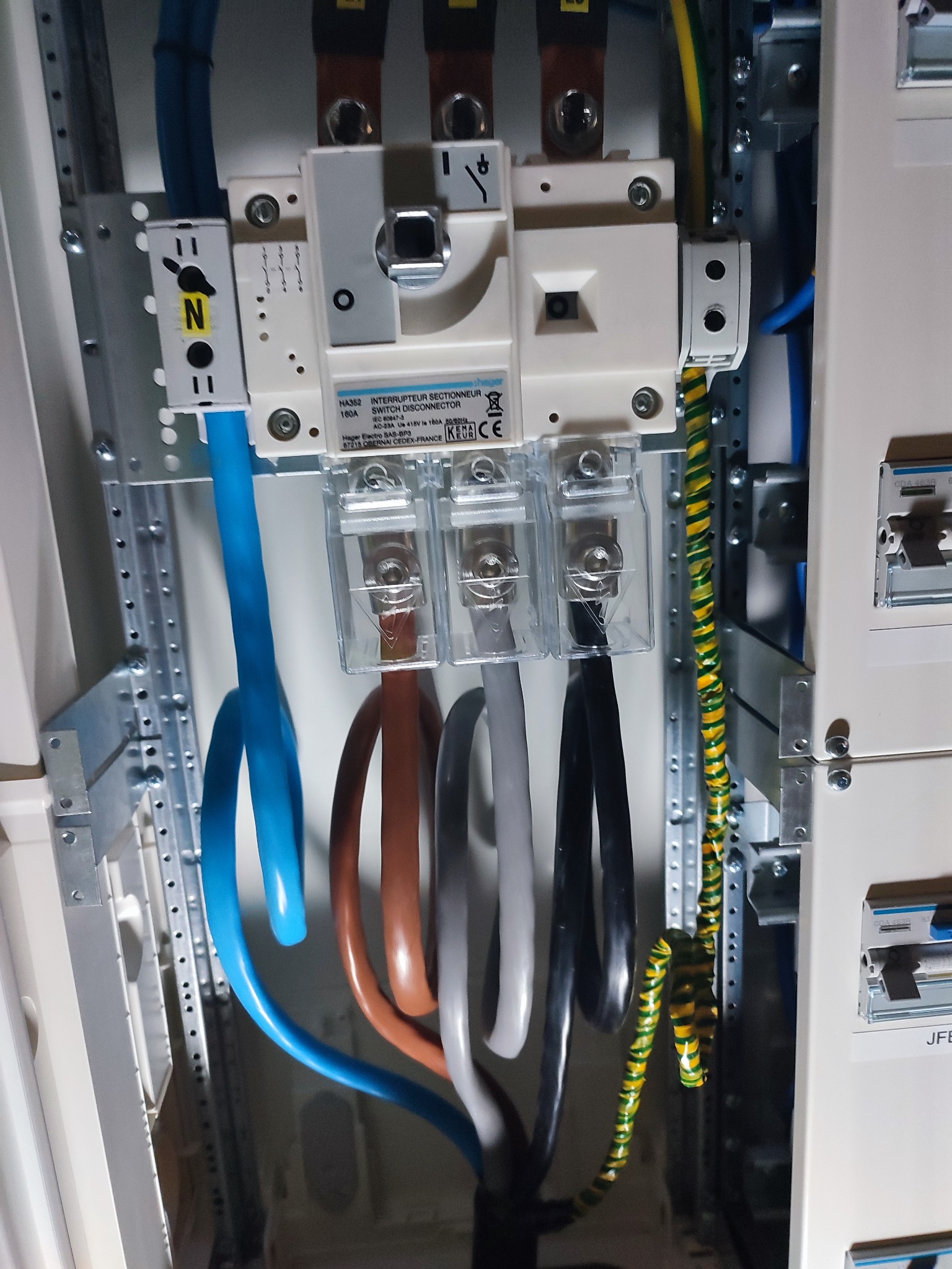 Rozdzielnica elektryczna z bezpiecznikiem i podłączonymi przewodami o różnych kolorach, w tym przewód uziemiający w żółto-zielonej izolacji. Widoczne elementy montażowe.