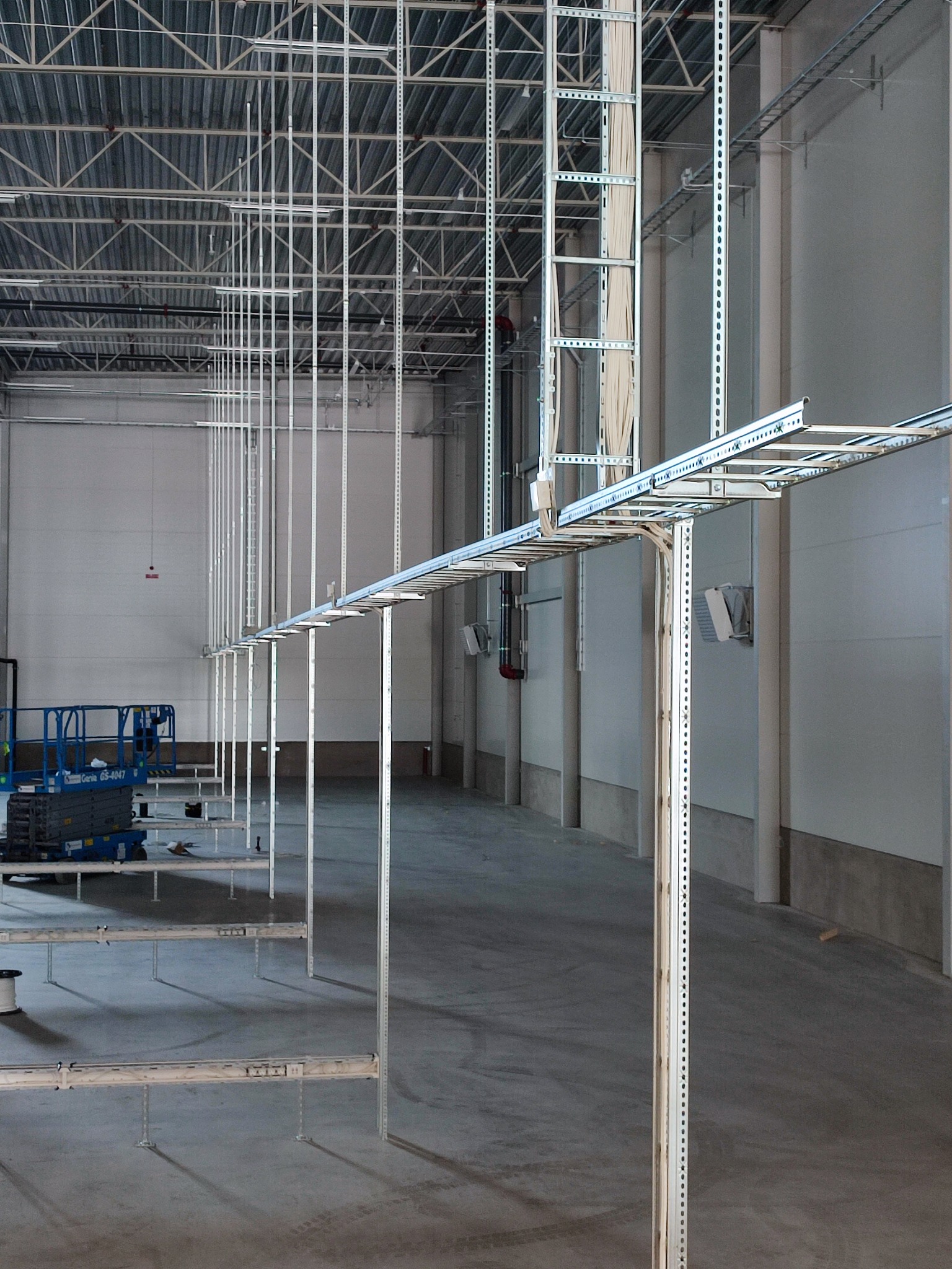 Nowoczesna instalacja kablowa w hali przemysłowej z wykorzystaniem drabinek kablowych i wsporników, widoczny podnośnik koszowy.