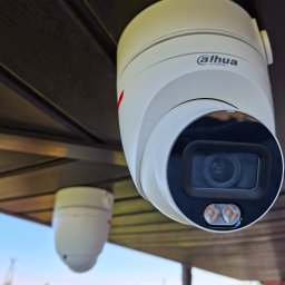 Smart Elektro Dawid Kowalski - Kamera monitoringu Dahua zamontowana pod dachem w Wielgiem, widok z dołu na obiektyw i fragment krajobrazu w tle. Nowoczesny system zabezpieczeń.