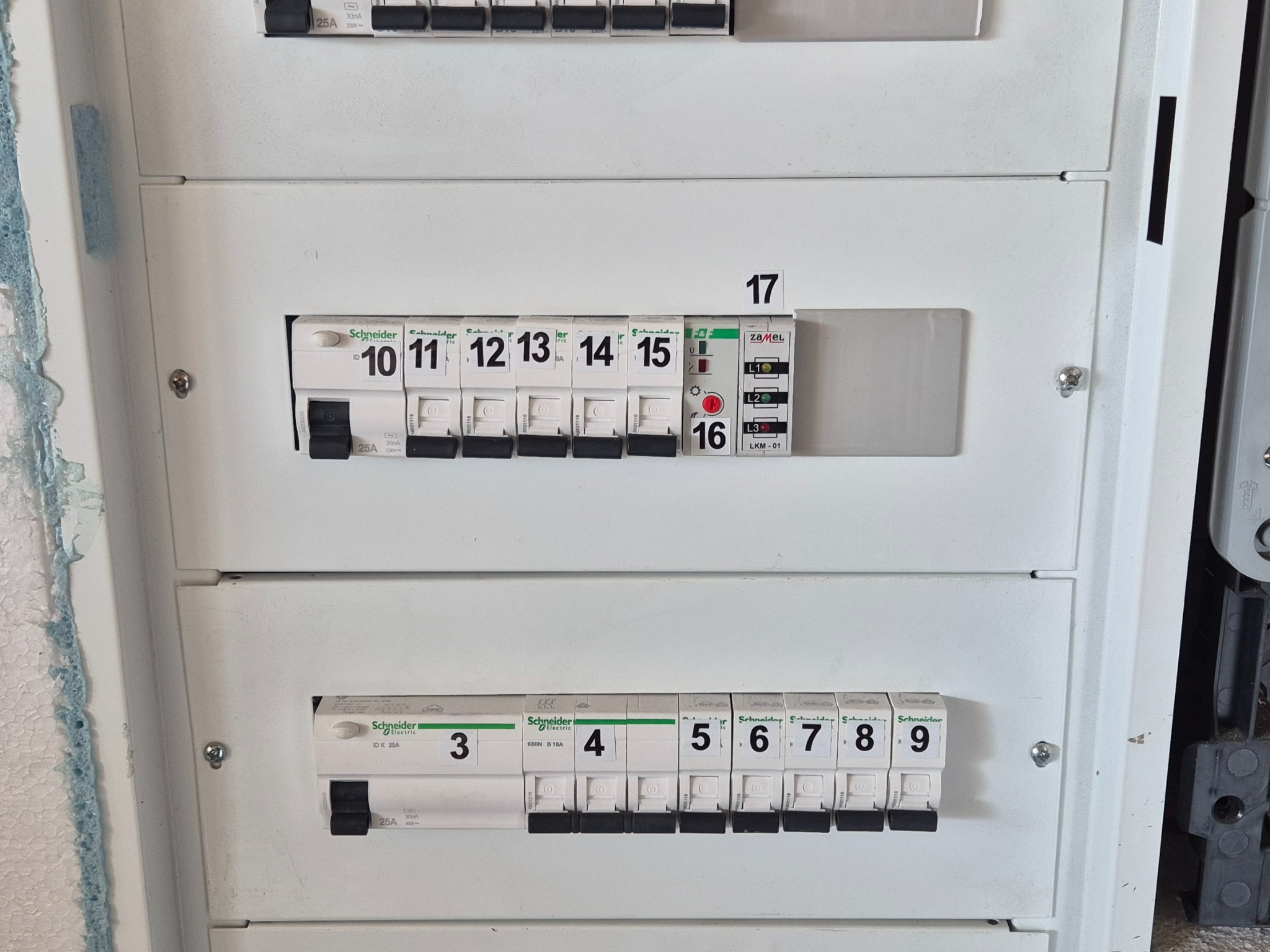 Rozdzielnica elektryczna z bezpiecznikami Schneider Electric, numery 3-17. Widoczne oznaczenia amperażu i napięcia. Biała obudowa, zbliżenie na aparaturę modułową.