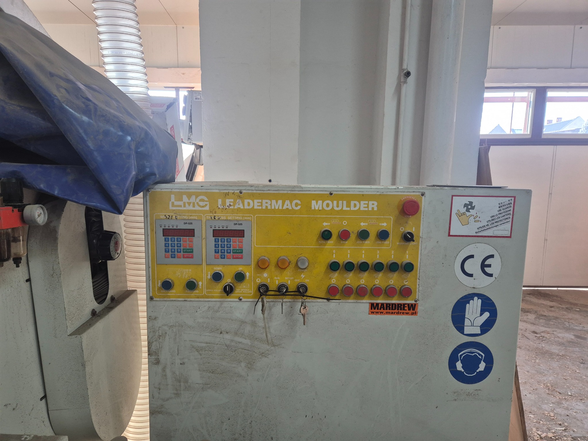 Szara, przemysłowa frezarka LMC LeaderMac Moulder z żółtym panelem sterowania, z widocznymi przyciskami, wyświetlaczami i naklejkami ostrzegawczymi. Częściowo zakryta plandeką.