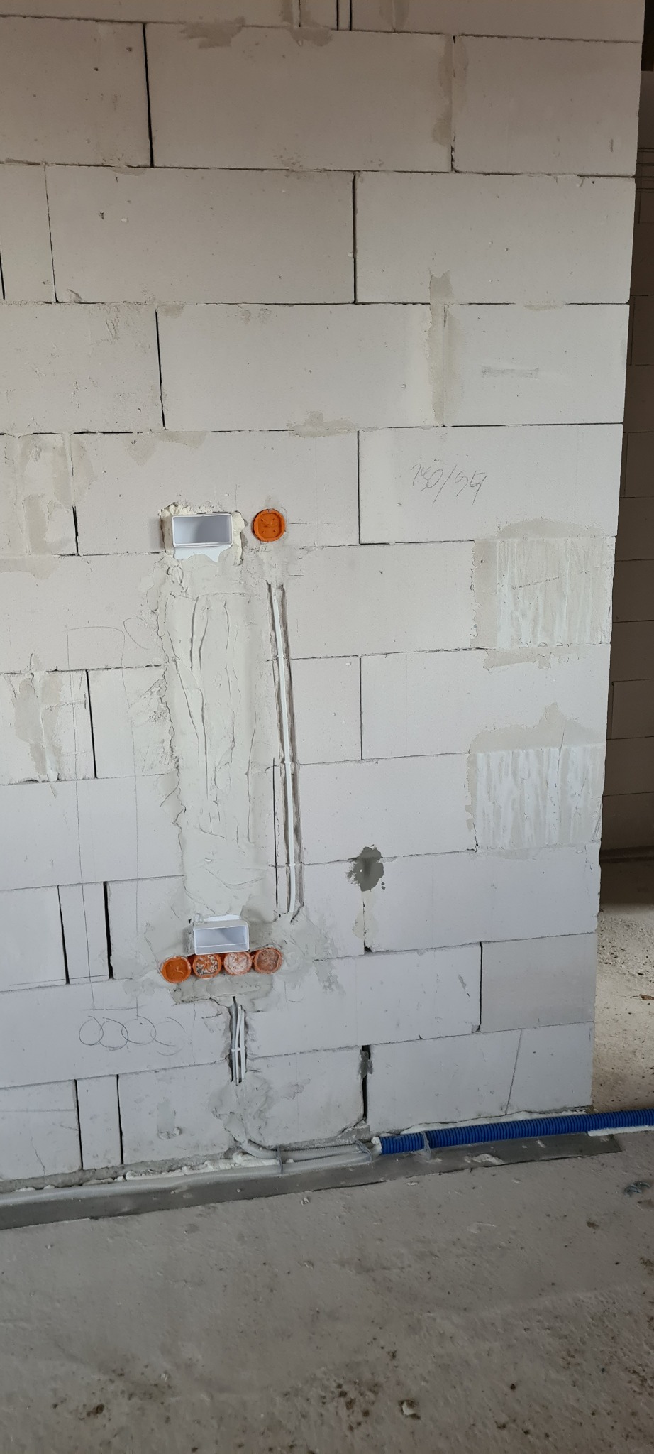 Ściana z betonu komórkowego z zamontowanymi puszkami elektrycznymi i rurami instalacyjnymi, gotowa do dalszych prac wykończeniowych.