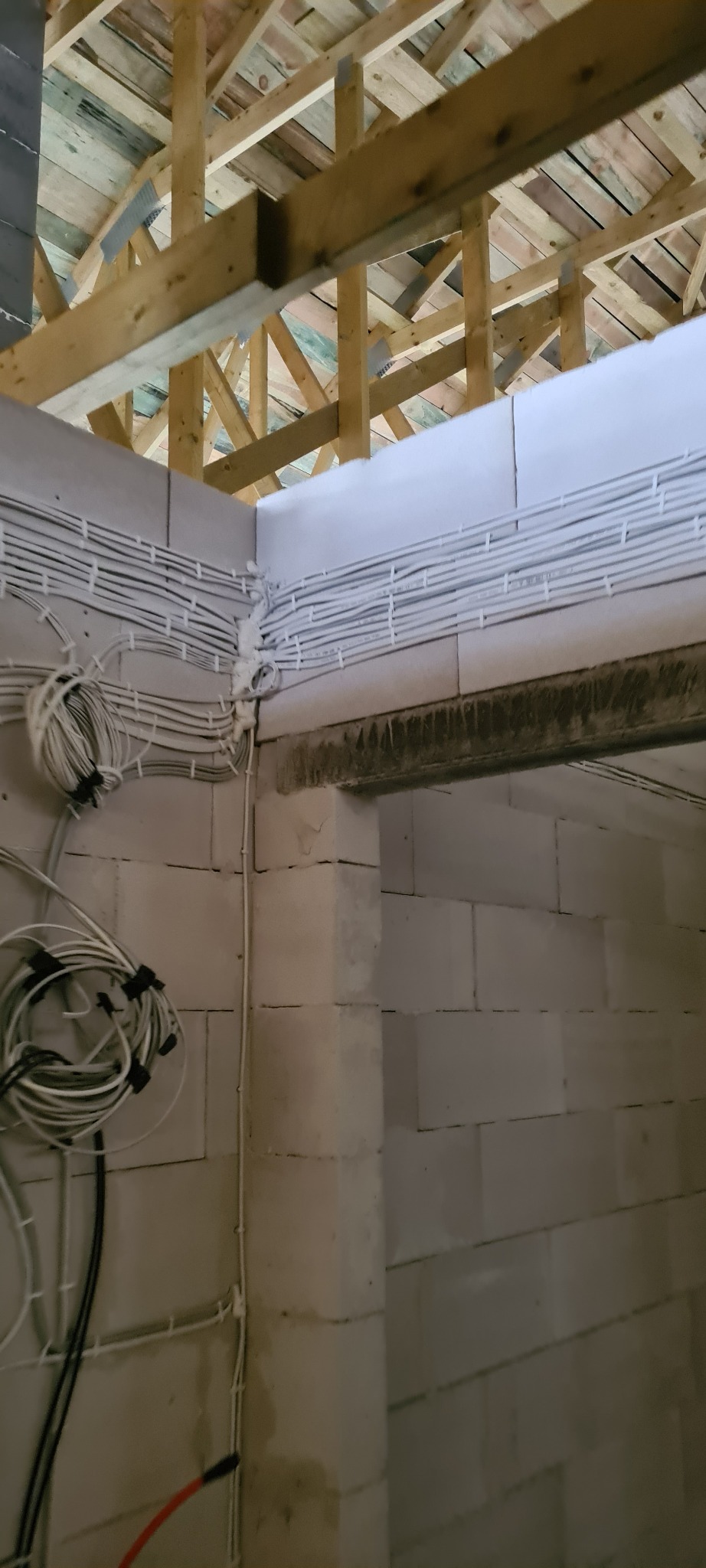 Instalacja przewodów elektrycznych w nowym budynku z drewnianą konstrukcją dachu. Kable prowadzone równolegle, zabezpieczone pianką montażową w narożnikach.