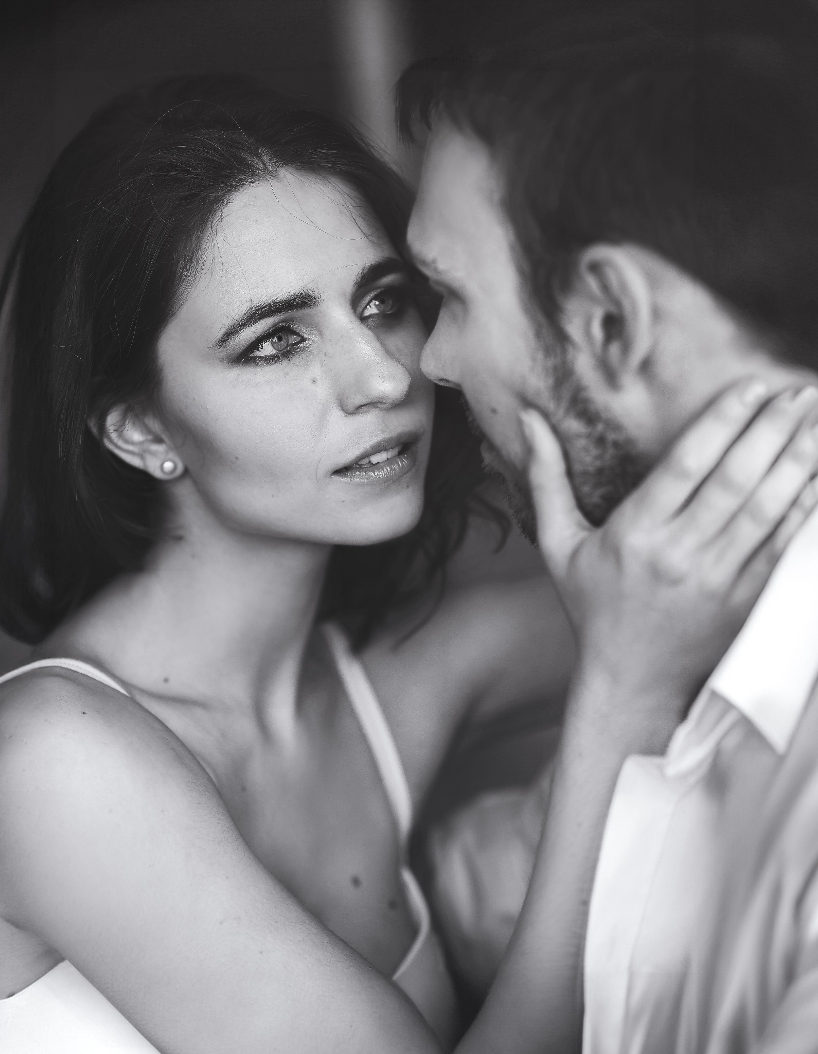 Portret pary w czerni i bieli, kobieta patrzy w górę na mężczyznę, który dotyka jej szyi. Delikatne światło, głębia ostrości skupiona na twarzach.