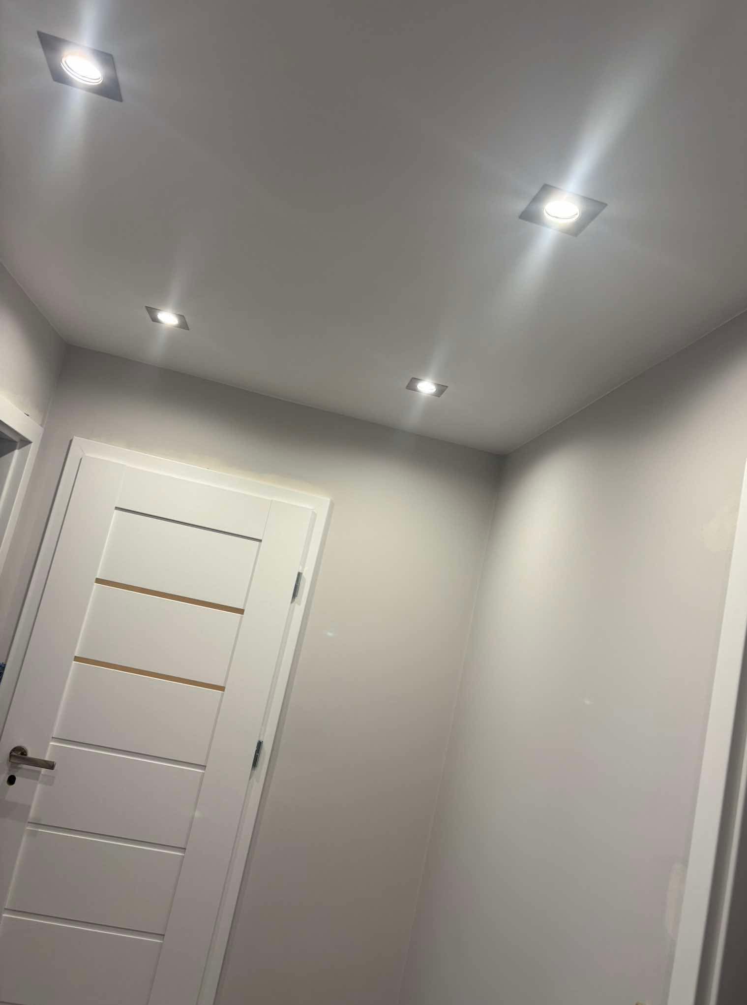 Białe drzwi wewnętrzne z poziomymi wstawkami, szara ściana i sufit z czterema punktowymi lampami LED. Minimalistyczne wykończenie wnętrza.