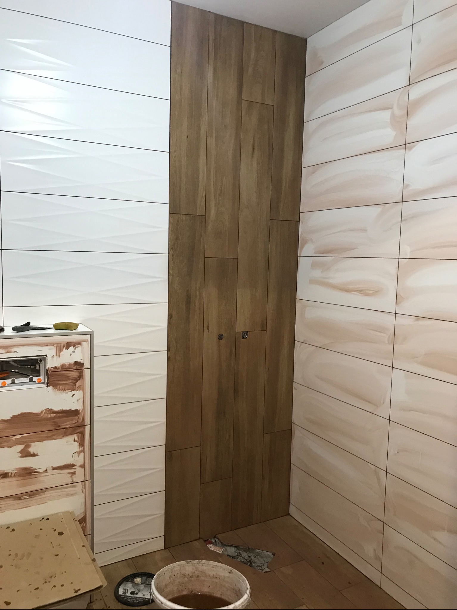 Łazienka po remoncie: ściany wyłożone różnymi płytkami - białe 3D, imitujące drewno i beżowe z wzorem. Na podłodze panele, widoczny fragment zabudowy WC.