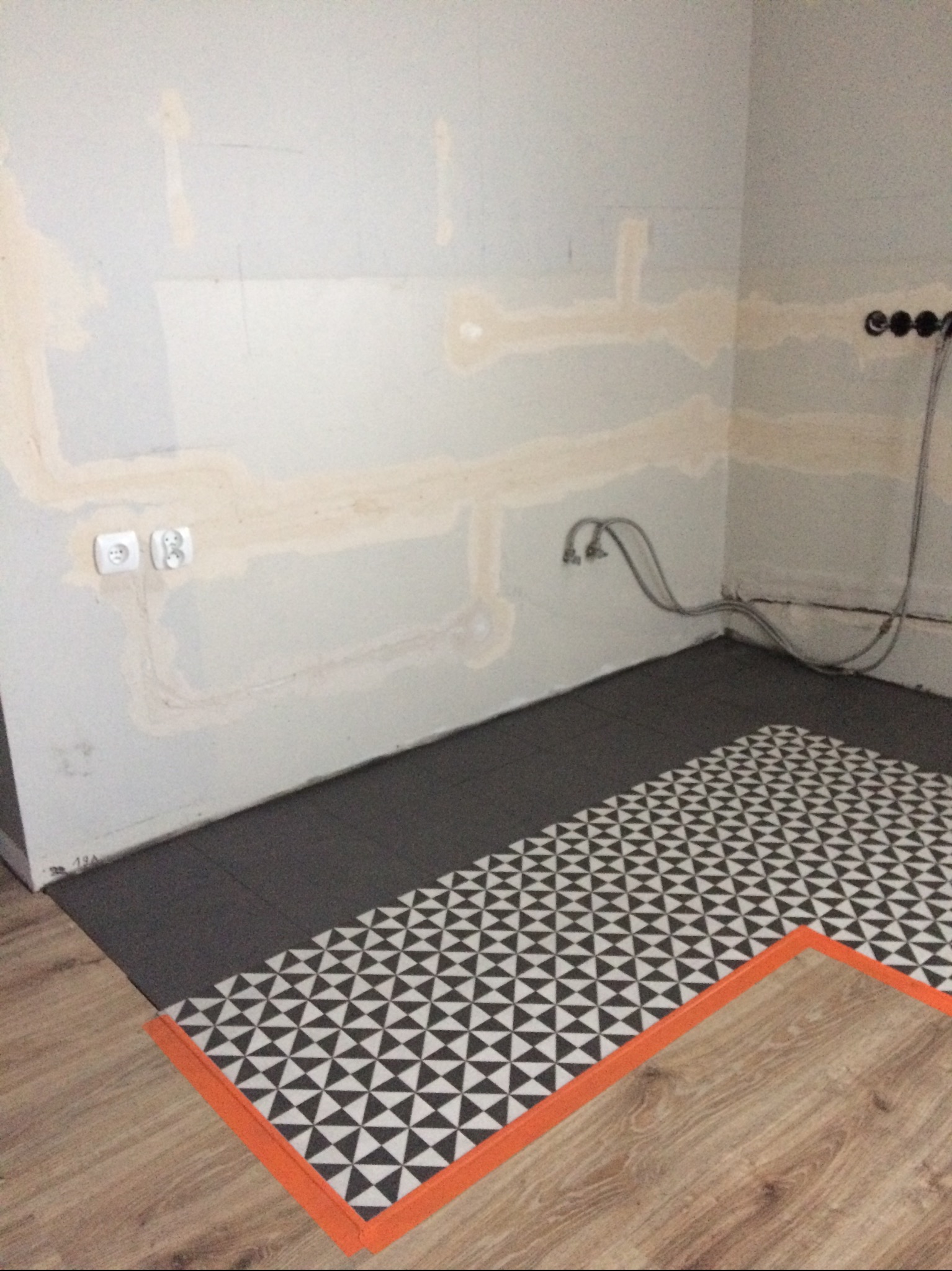 Fragment łazienki w trakcie prac wykończeniowych: położona część płytek podłogowych z wzorem, przygotowane ściany z wyprowadzonymi instalacjami.