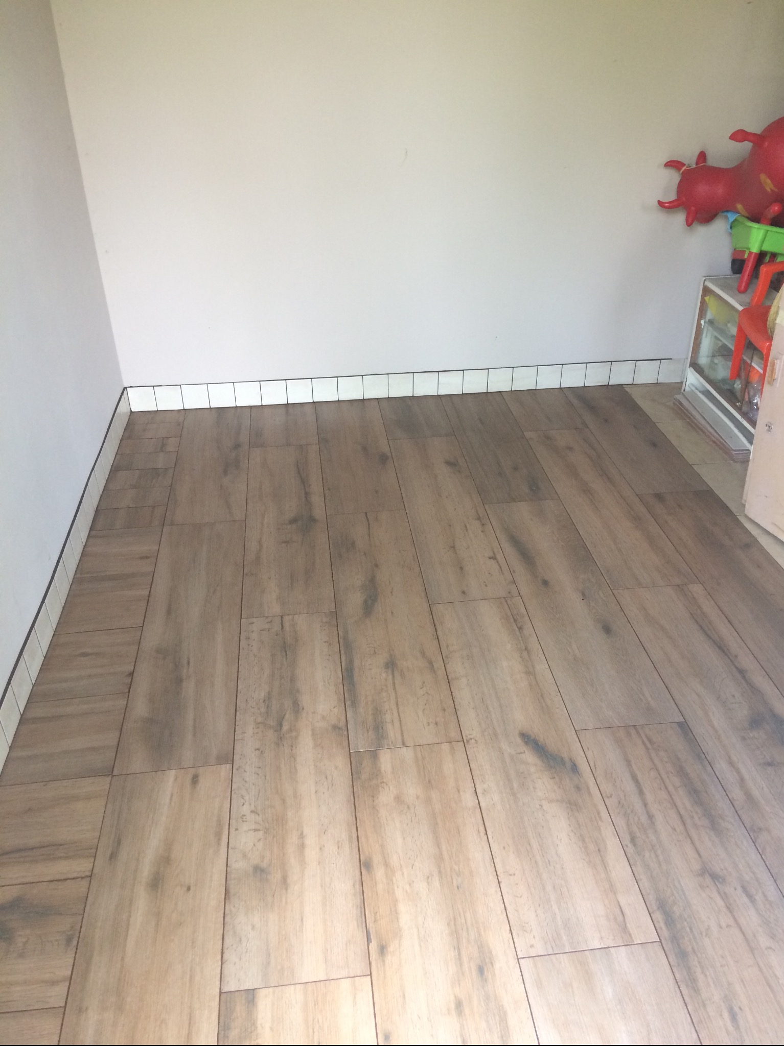 Ukończona podłoga z paneli imitujących drewno, z białymi płytkami przypodłogowymi. W tle zabawki dziecięce,  widok z perspektywy podłogi.