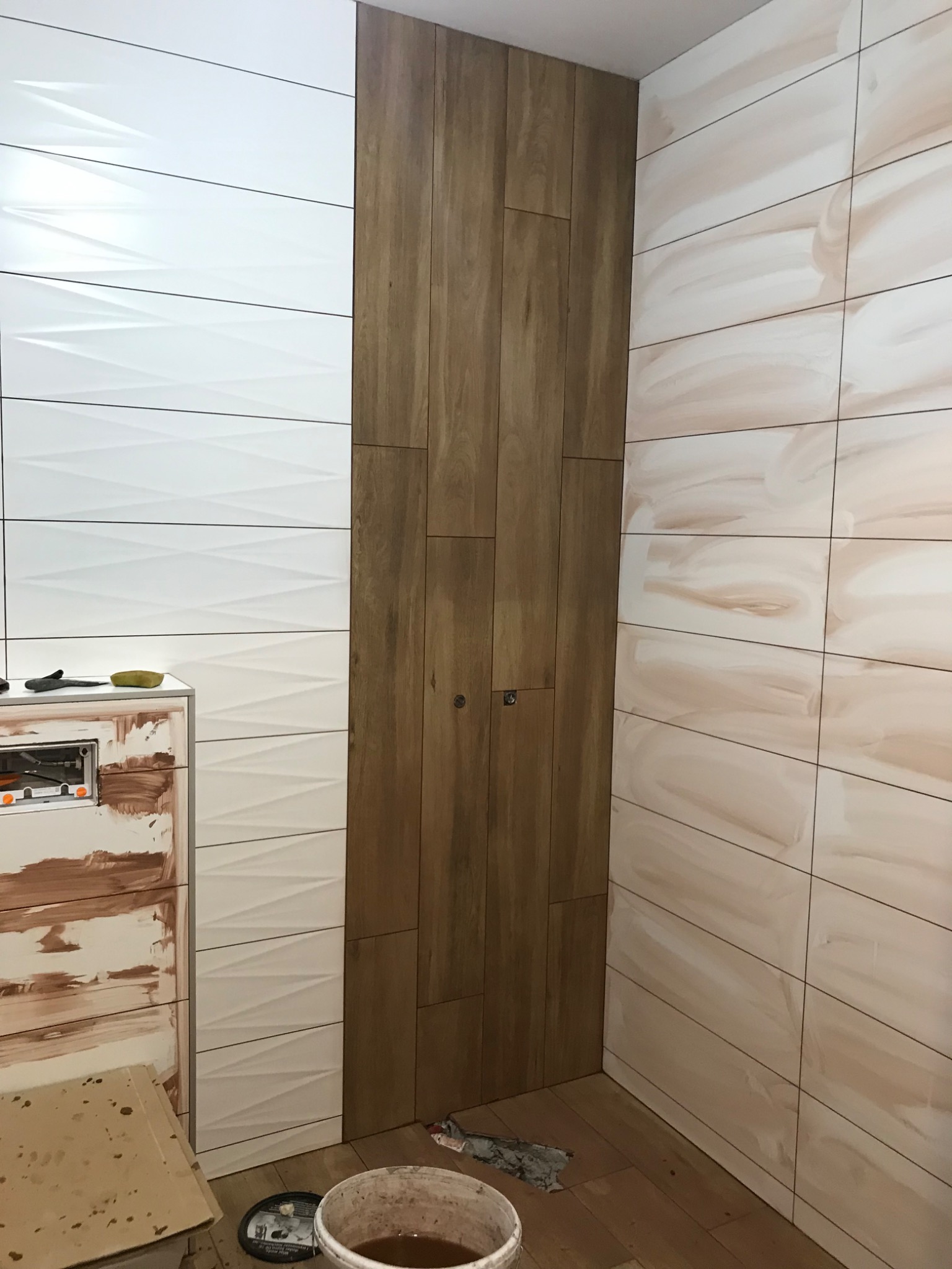 Układanie płytek w łazience w Miłoszycach: ściany wyłożone płytkami imitującymi drewno i białymi z geometrycznym wzorem. Umywalka w trakcie montażu.