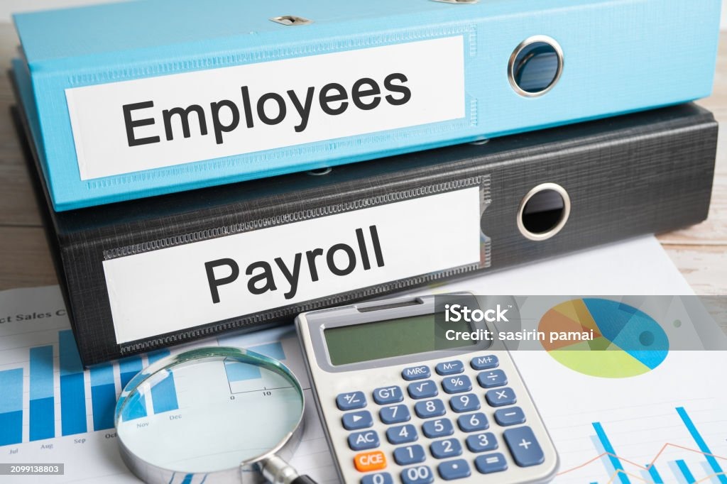 Dwa segregatory: błękitny z napisem 'Employees' i czarny z napisem 'Payroll'. Kalkulator i lupa leżą na wykresach.