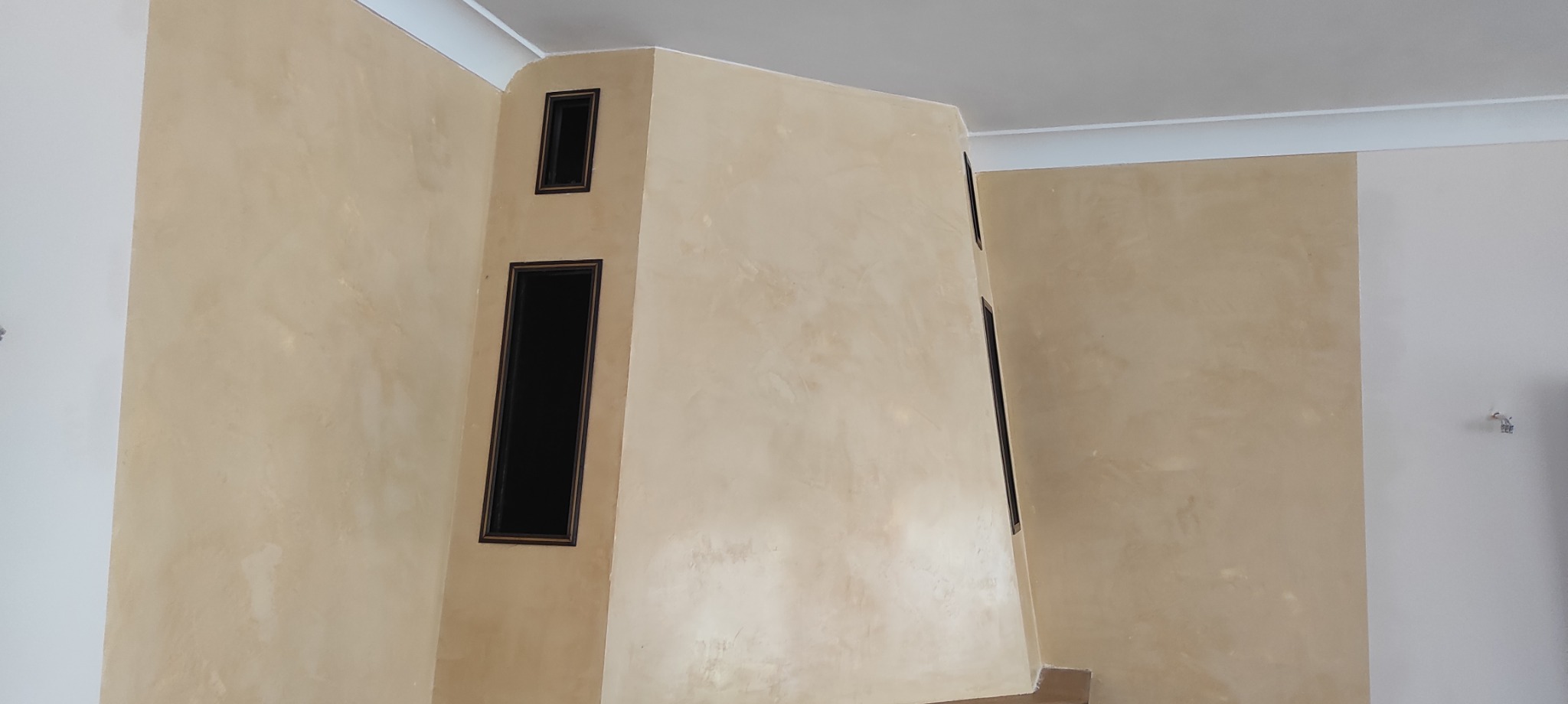 Ściana z beżową, dekoracyjną strukturą i wnękami z czarnymi obramowaniami, widok z dołu, fragment wnętrza po pracach wykończeniowych.
